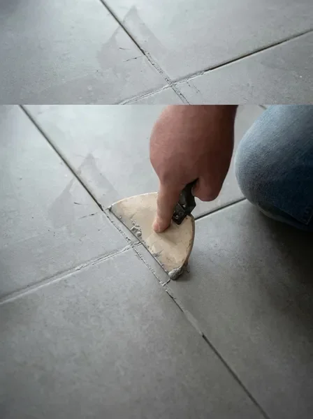 Person's hand applying grey grout between light grey floor tiles with a small trowel.